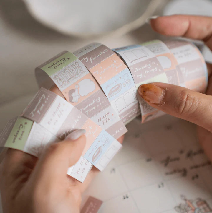 Hands unrolling pastel Stationery Lover Label Sticker Tape with book and note icons