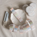 Flat lay of pastel “stationery lover” washi tape rolls and unrolled strips arranged around a ceramic dish, with a utility cutter nearby.