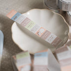 Single strip of soft pastel washi tape laid across a ceramic plate, showing journaling and stationery-inspired illustrations and text labels.