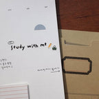 Notebook with 'Study with me' text and a brown folder on a wooden surface