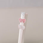 Two decorative clips with pink bows on a white stick against a beige background