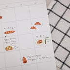 Calendar sheet with food-themed stickers on a checkered fabric background