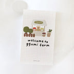 Grid-patterned towel with cartoon bear and vegetable stand design, text 'welcome to ggumi farm', on a white background.