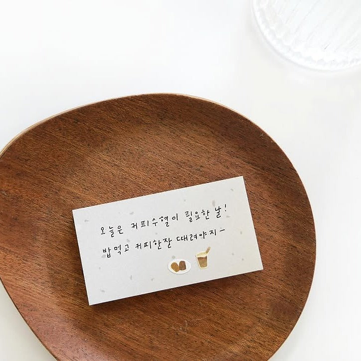 Wooden plate with a white card featuring Korean text and illustrations on a white background