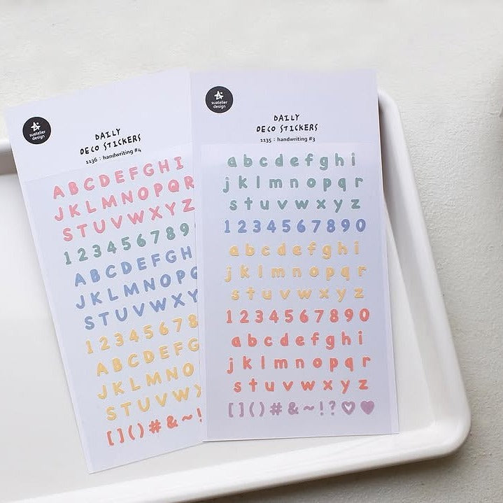 Two sheets of colorful letter and number stickers on a white tray.