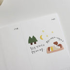 White fabric with embroidered design of two dogs on a blanket, trees, and stars.