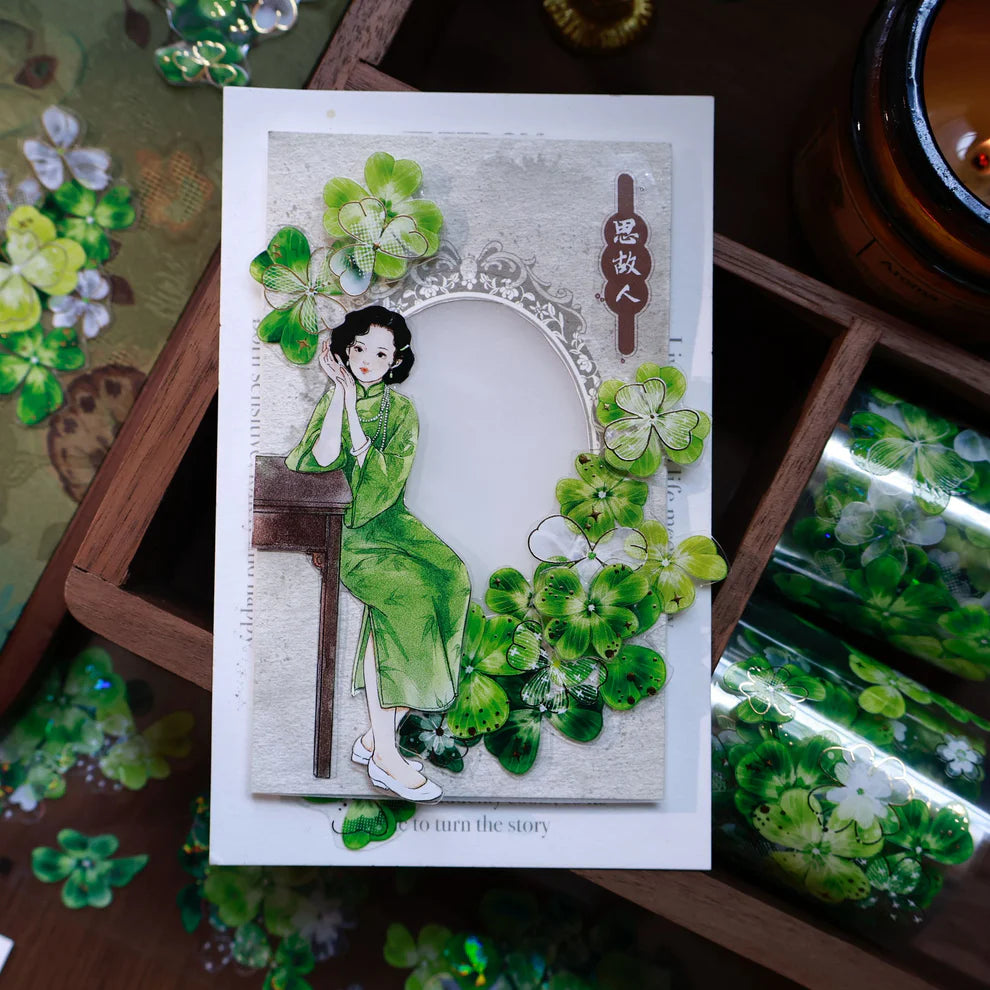 Card with a design of a woman in a green dress surrounded by green flowers on a wooden surface.