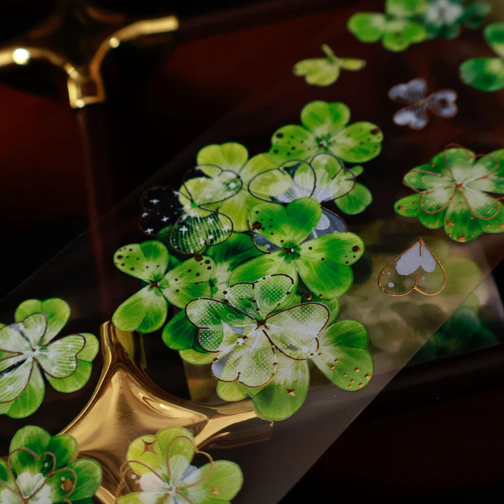 Green four-leaf clover stickers on a reflective surface with a gold object in the background.