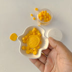 Hand holding a white mold with yellow candy pieces on a light gray background