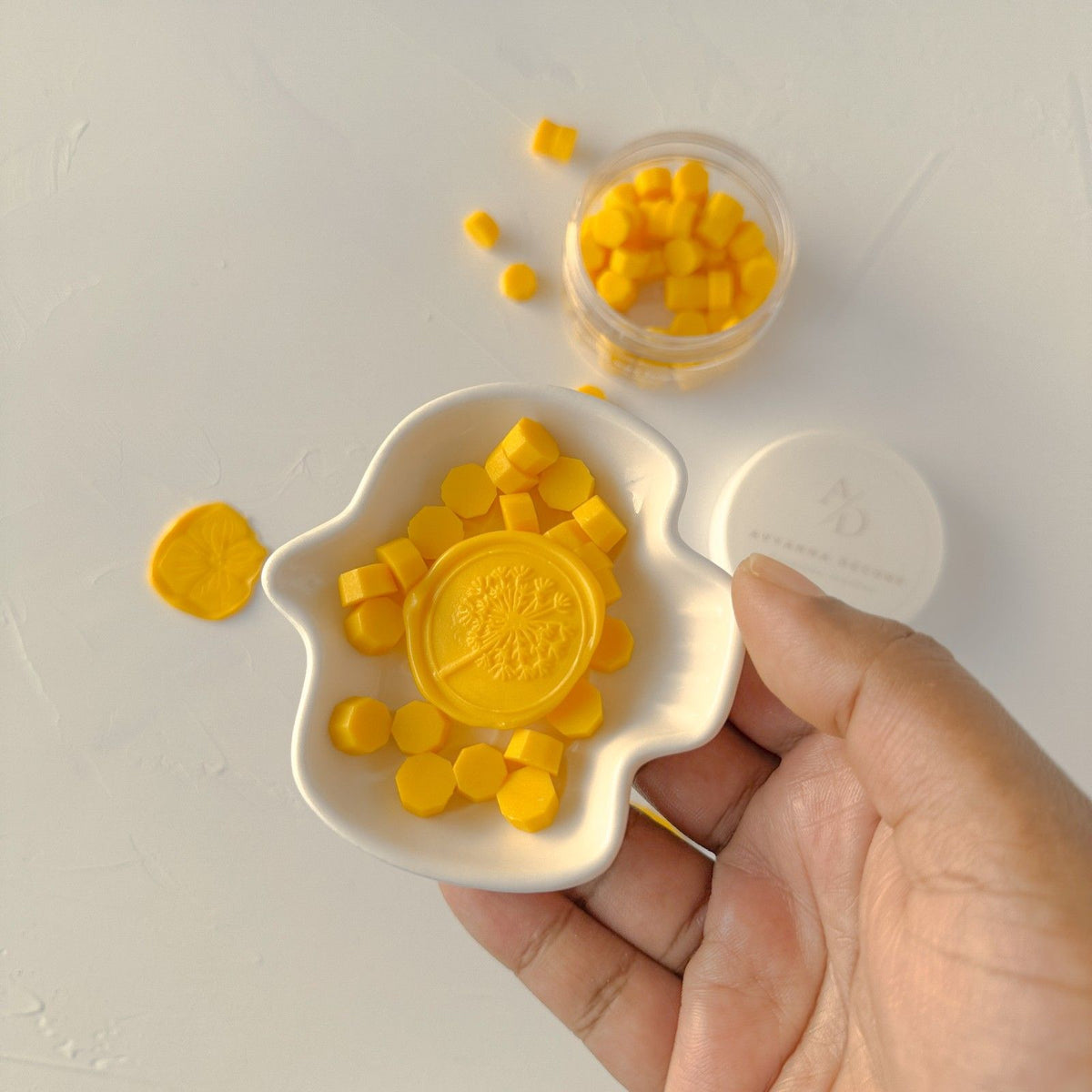 Hand holding a white mold of Sunny Pumpkin Wax Beads in a bright pumpkin-orange shade on a light grey background