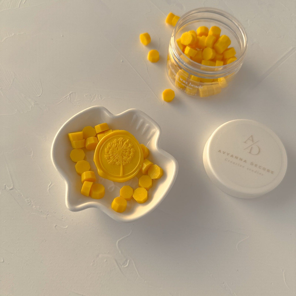 Sunny Pumpkin sealing wax beads in a white heart-shaped dish and clear container on a light grey backdrop