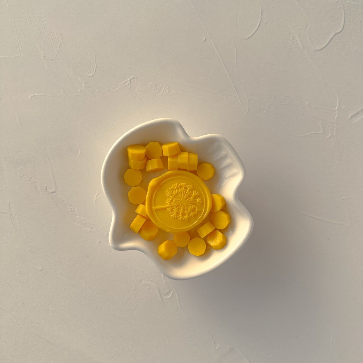Shell-shaped white dish filled with Sunny Pumpkin Wax Beads in a warm orange tone, top view on soft grey