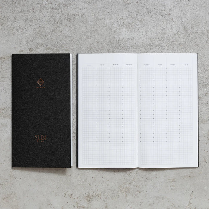 Take A Note Slim Weekly Planner closed in black beside an open grid spread on concrete