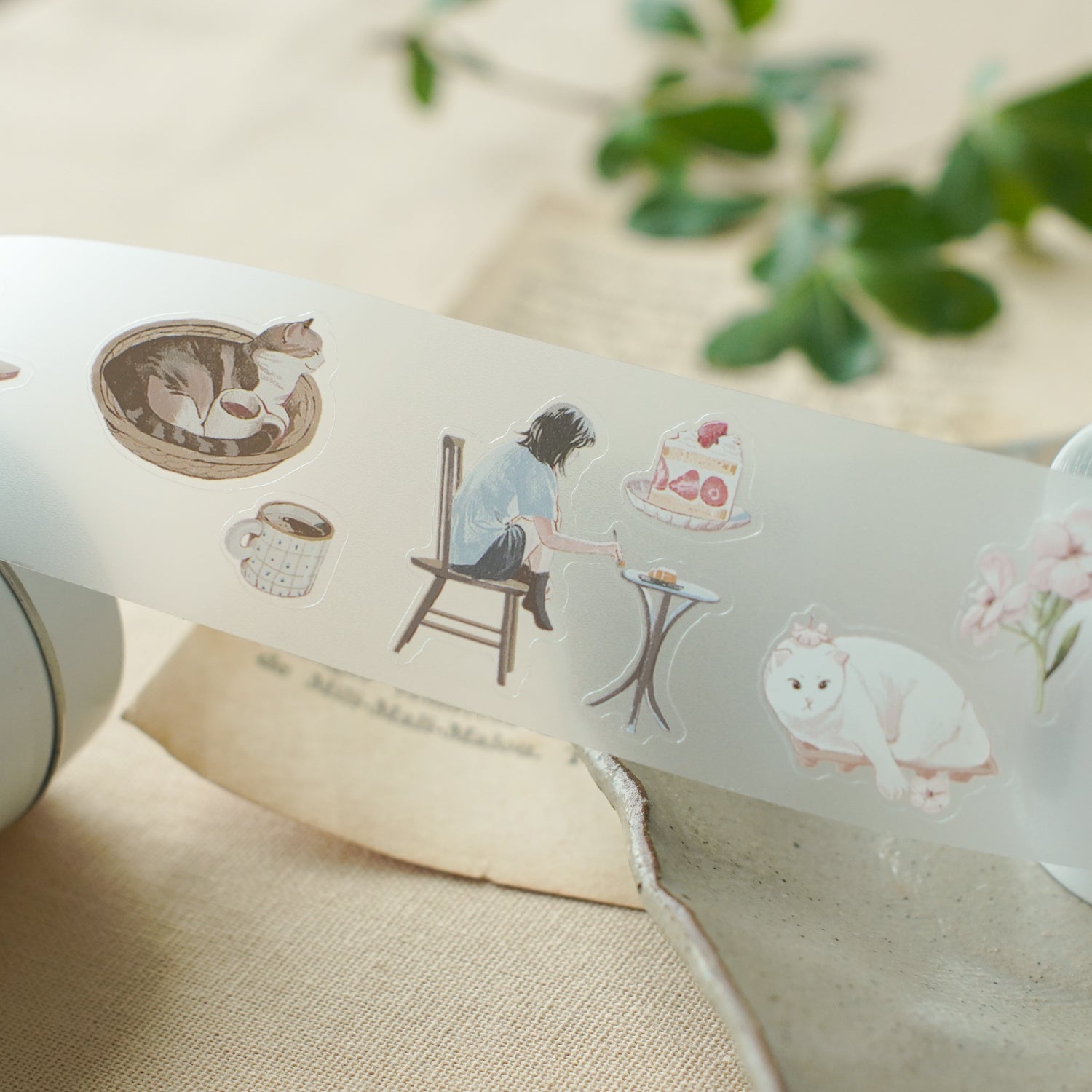 Decorative tape with illustrations of a woman, a cat, and a cake on a beige surface.