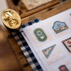 Gold stamp on a sheet of decorative stamps with various designs on a wooden surface.
