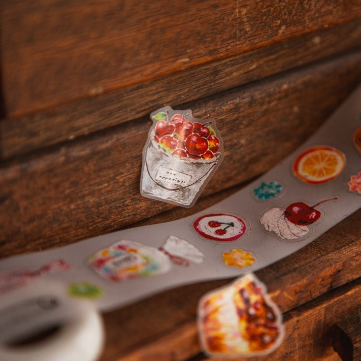 Strip of The Gift PET Tape fruit-themed stickers displayed on a wooden surface, detail view