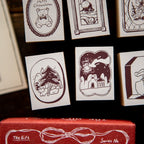 Collection of illustrated cards with various designs on a dark background, featuring a red box with 'The Gift' design.
