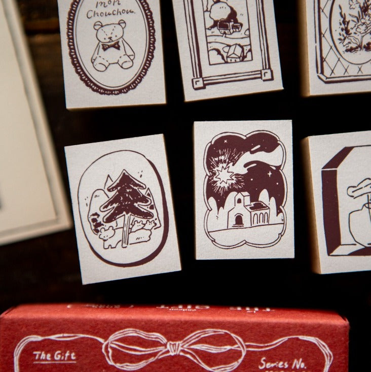 Collection of illustrated cards with various designs on a dark background, featuring a red box with 'The Gift' design.