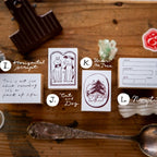 Collection of vintage-style cards and stationery items on a wooden surface with a spoon and camera lens.