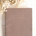 Brown notebook with 'the memory keeper' on a light background with dried flowers.