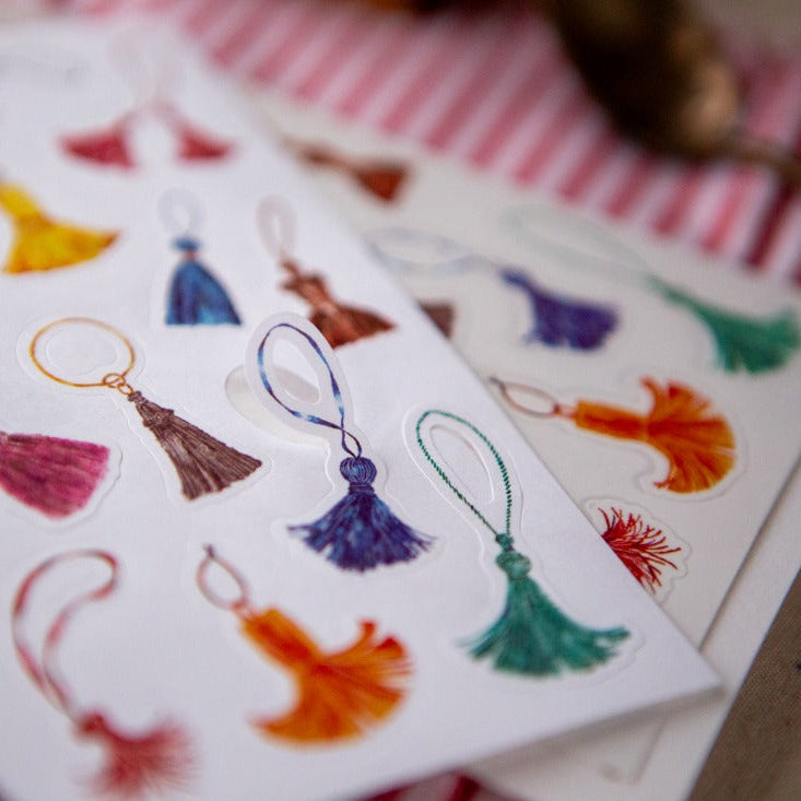 The Tassel Sticker Pack earring-style tassel designs on a white card over stripes