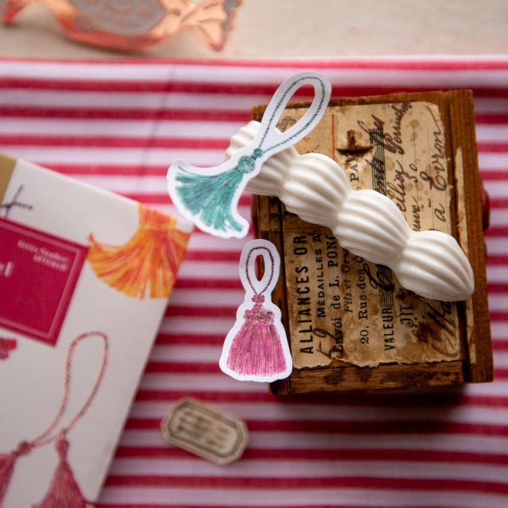 The Tassel Sticker Pack tassel design with vintage-style packaging on striped fabric