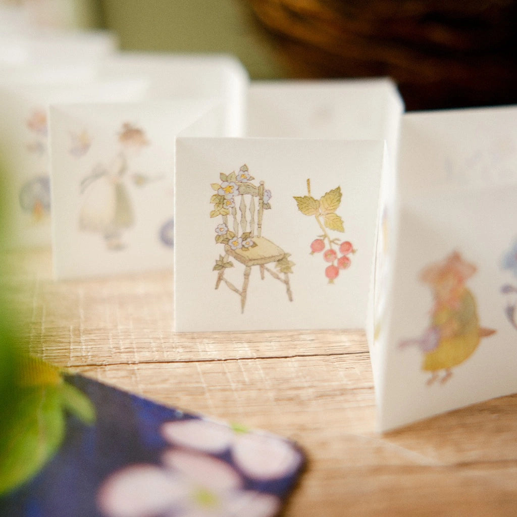 Small square card with illustrations of a chair, butterfly, and flowers on a wooden surface.
