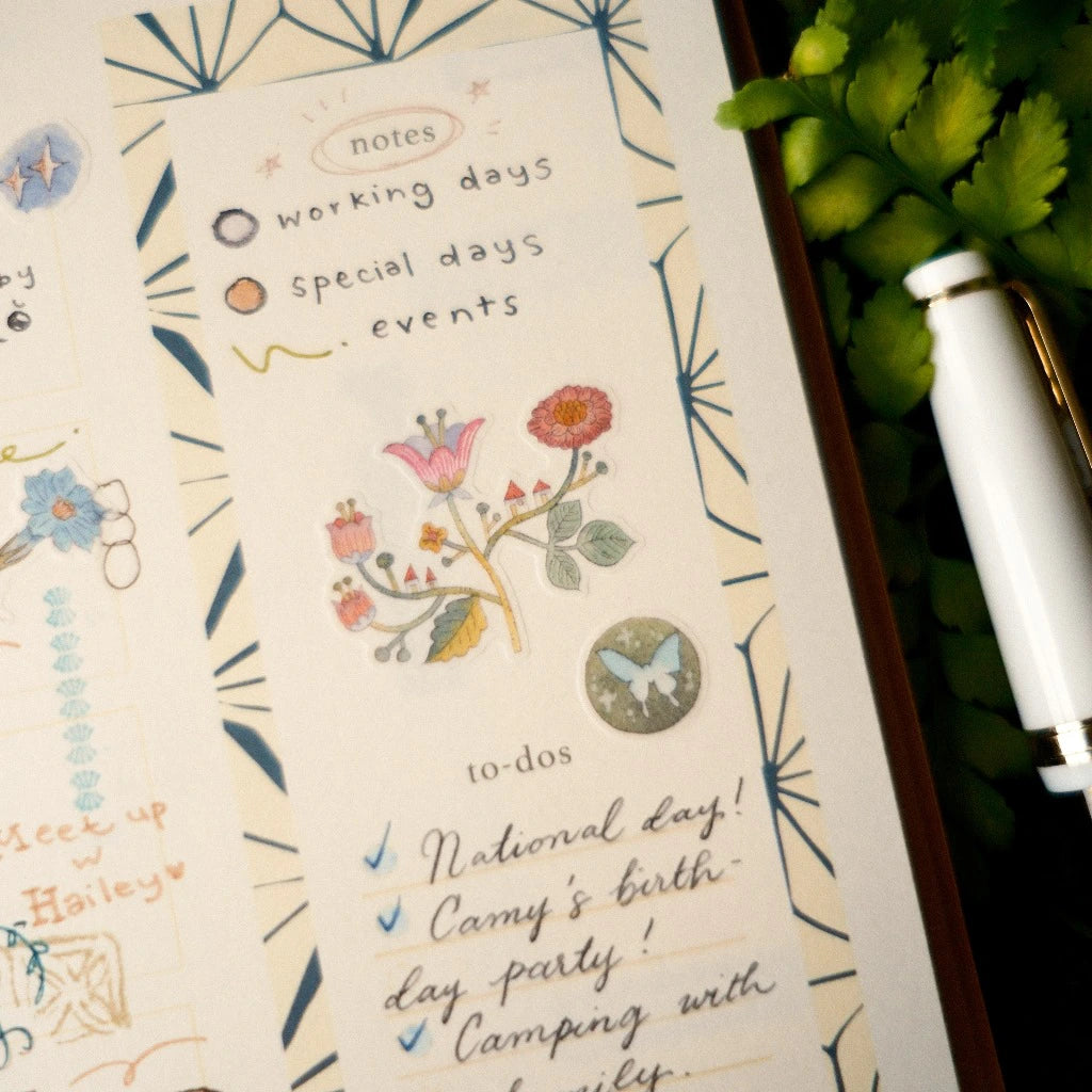 Notebook with decorative pages and a pen on a green leafy background