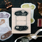 Wooden stamp with 'Silk & Ribbon' design on a dark surface with ribbons and paper.