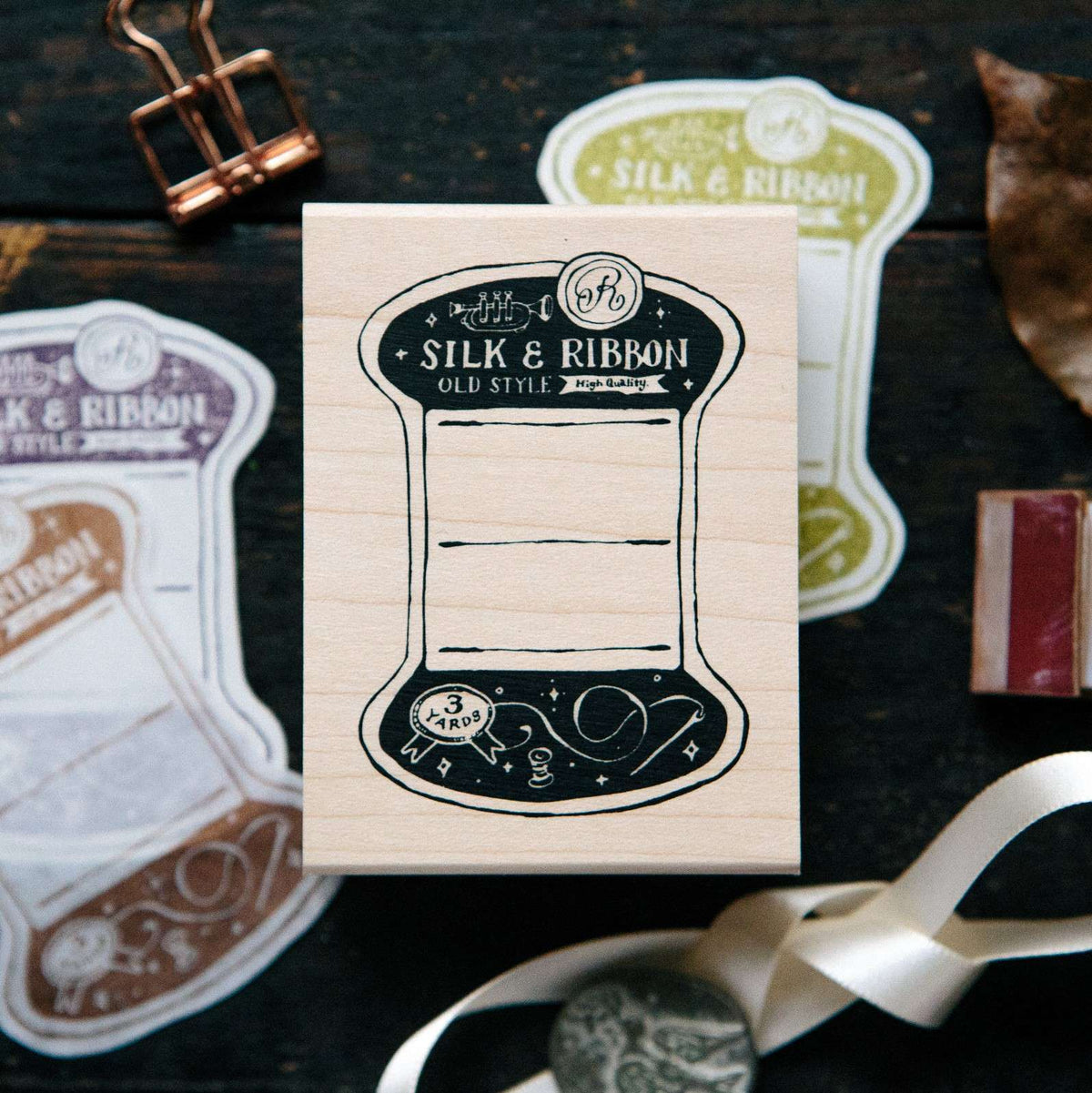 Thread Card Rubber Stamp with Silk and Ribbon spool design among ribbons on dark wood