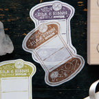 Sticker of a spool of silk and ribbon on a dark wooden surface