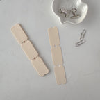 Beige paper clips on a gray surface with a white dish containing small metal items.