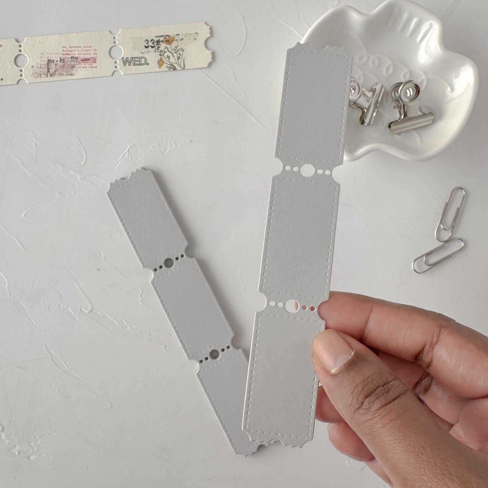 Hand holding a metallic strip with cut-out shapes on a light gray background