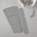 Set of gray cardstock tags with a scalloped edge on a light gray surface.