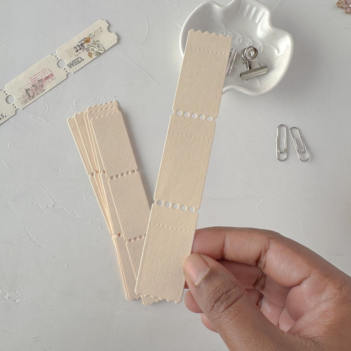 Hand holding cream Ticket Card Vol. 2 strips with a heart-shaped clip on light grey