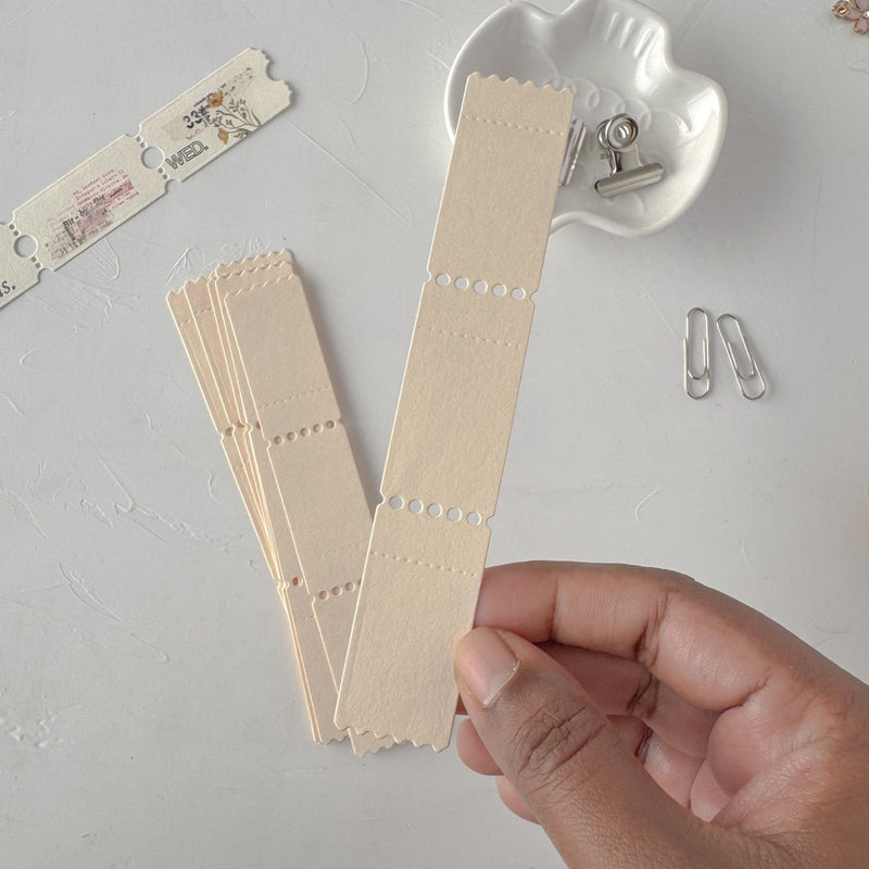 Hand holding cream Ticket Card Vol. 2 strips with a heart-shaped clip on light grey
