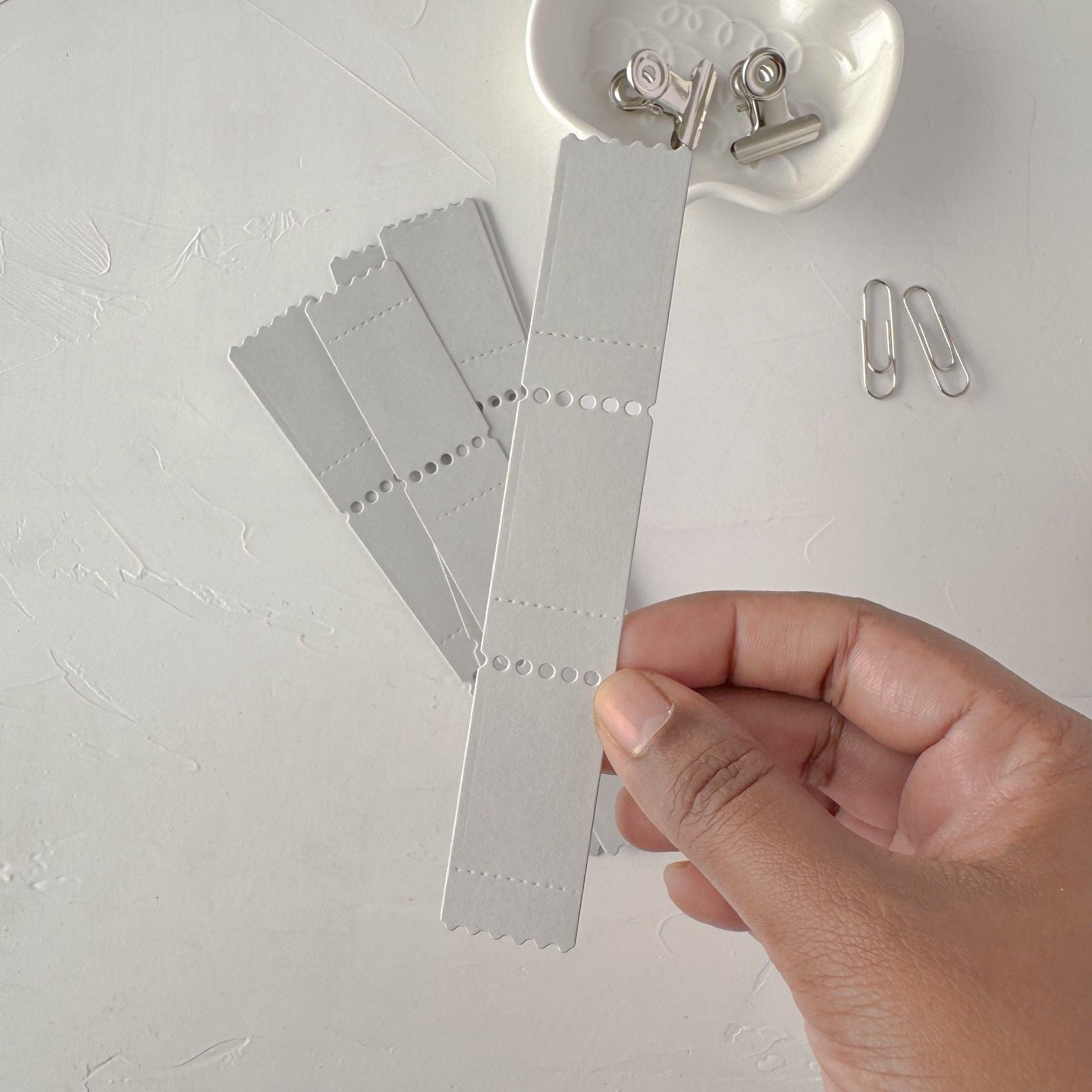 Hand holding up grey Ticket Card Vol. 2 label ephemera cards against a white background