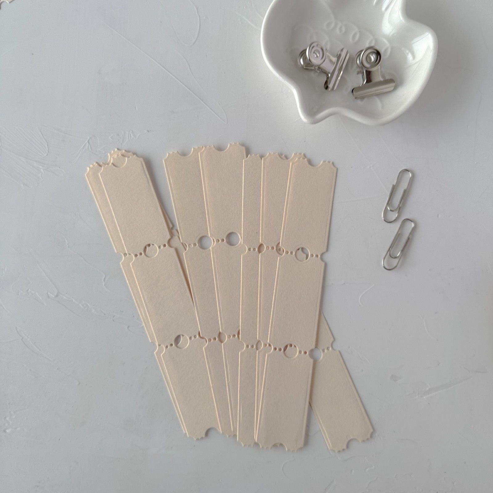 Beige paper strips with cut-out designs on a gray surface with metal clips.