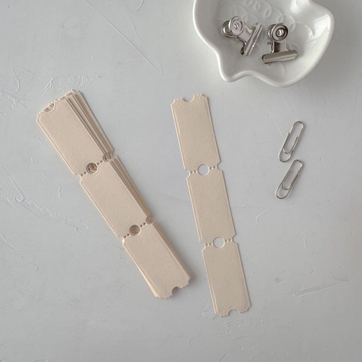 Cream Ticket Card Vol. 3 strip styled together with metal clips on a grey surface
