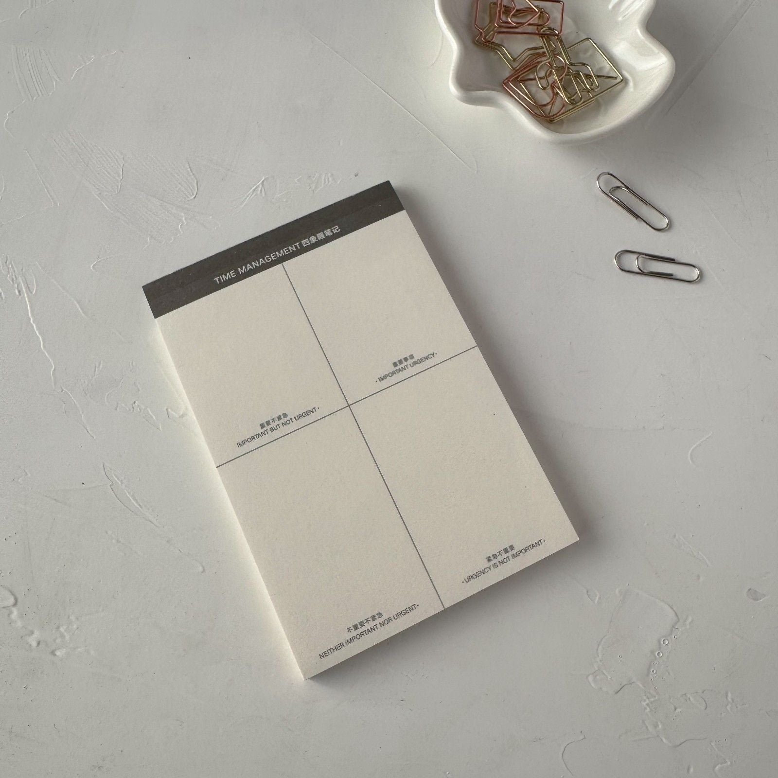 Notebook with time management layout on a gray surface with paper clips.
