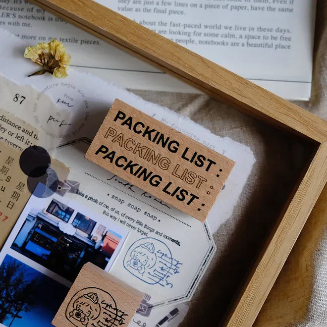 Packing list card with a wooden frame and dried flower on a textured surface