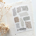 Sheet of patterned stickers on a textured surface with dried flowers.