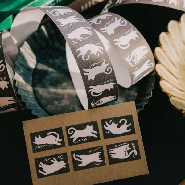 Rolls of Twisty Cats Label Sticker Tape with twisting cat designs on a black surface
