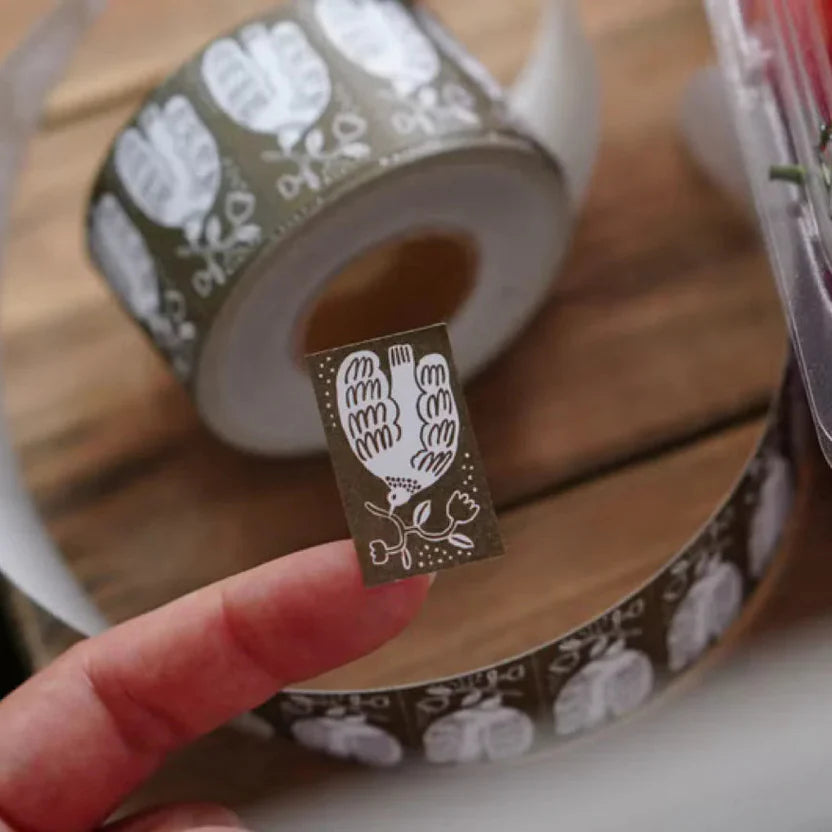 Roll of decorative tape with a hand-printed design held by a hand on a wooden surface.