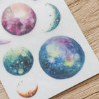 Sticker sheet with colorful planet designs on a wooden surface