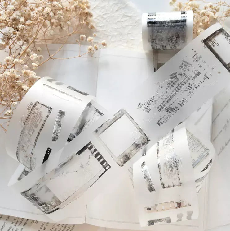 Rolls of Untold PET Tape with newspaper print designs and dried flowers on a white surface