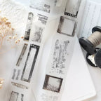 Collection of black and white printouts on a light surface with a spool of thread and dried flowers.