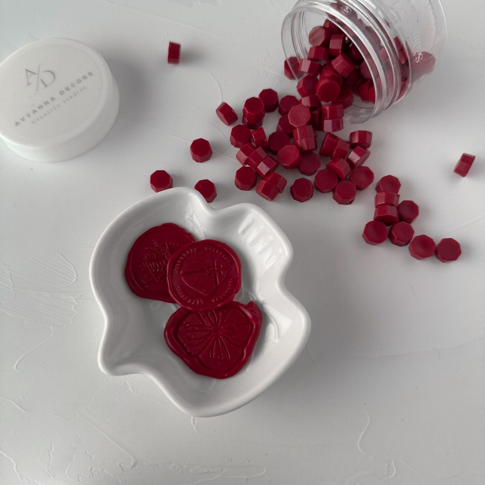 Red heart-shaped candies in a white dish with a jar of candies on a light gray background.