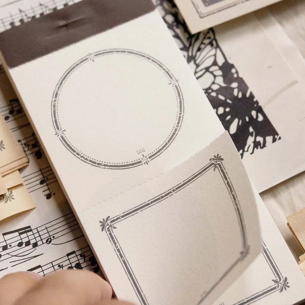 Hand holding a Vintage Frame Label Memo Pad sheet over music notes and stationery items