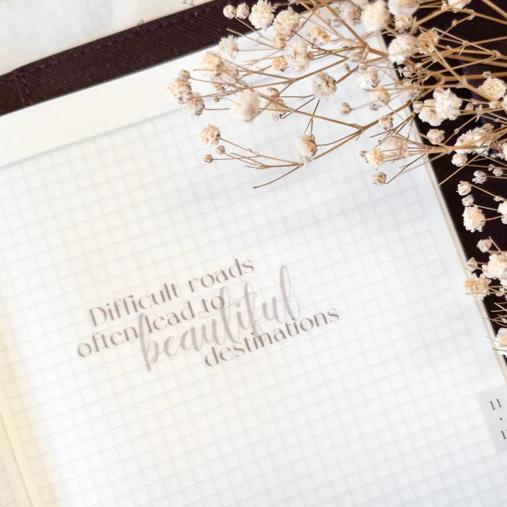 Beautiful Destinations quote sticker on a closed book with dried flowers on white